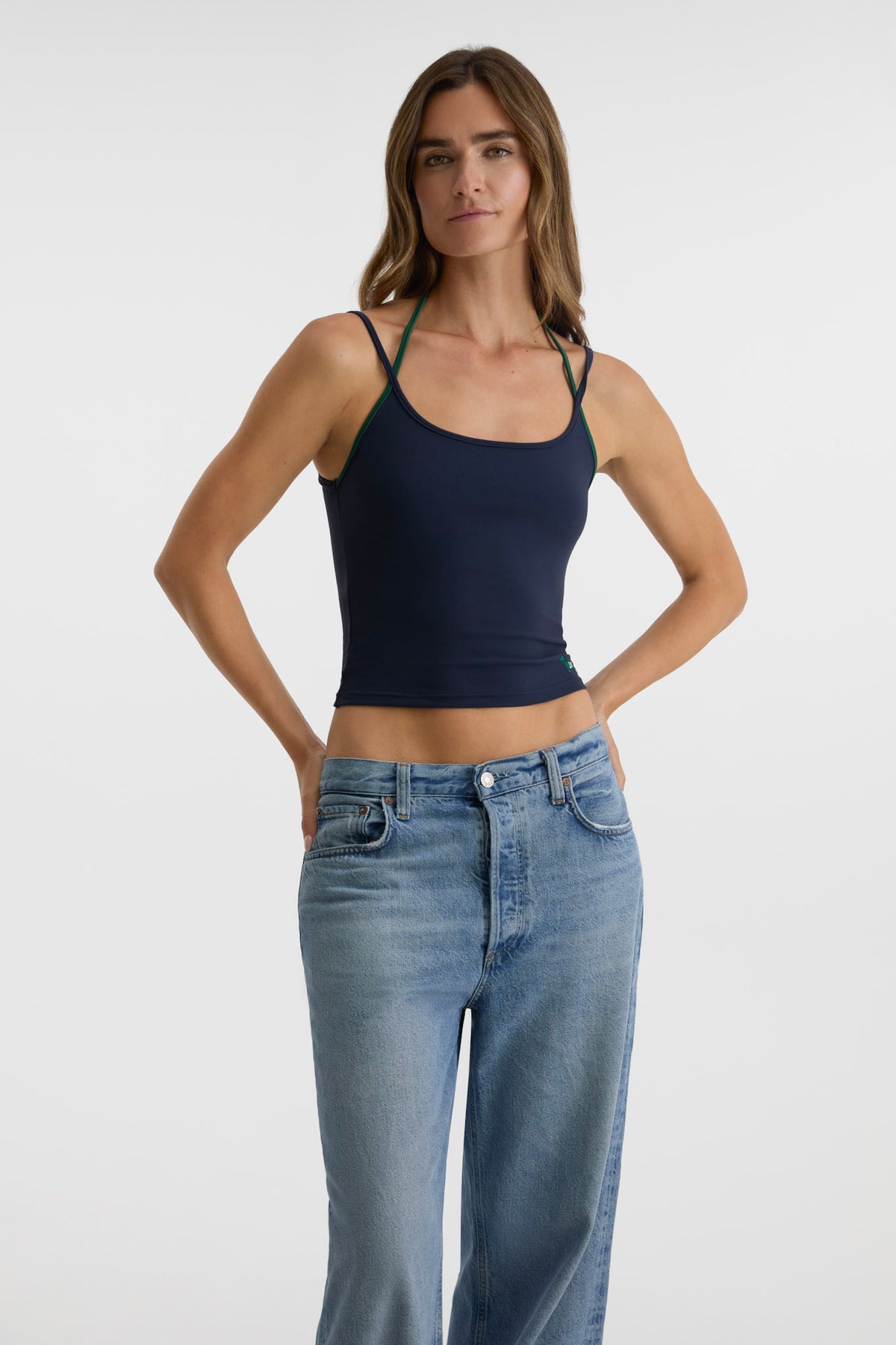 A woman modeling a navy blue tank top paired with light-wash blue jeans, standing against a light gray studio background.