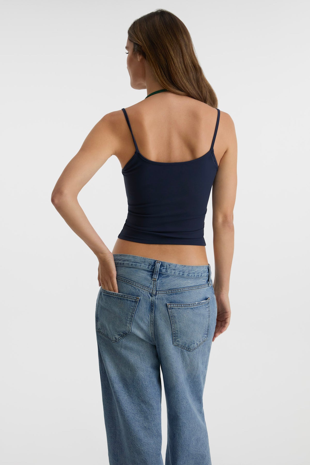 A woman shown from the back wearing a dark navy blue tank top and light blue jeans against a plain light gray studio background.